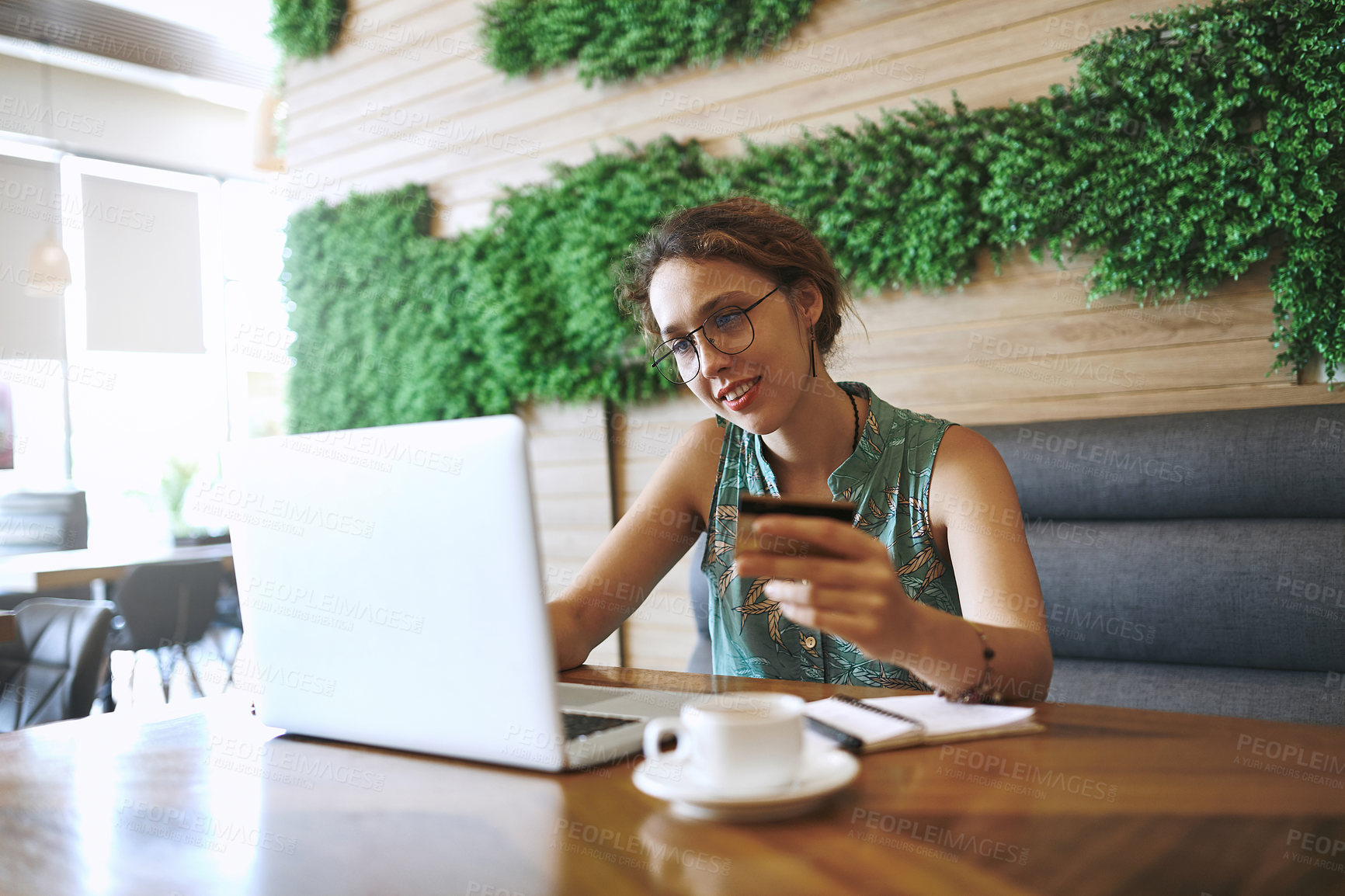 Buy stock photo Shot of a young woman using a laptop and credit card while working at a cafe