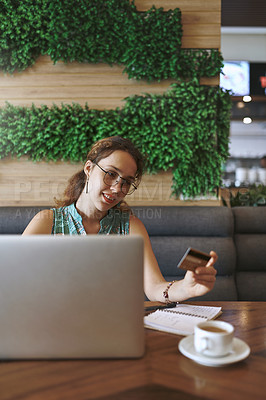 Buy stock photo Shot of a young woman using a laptop and credit card while working at a cafe