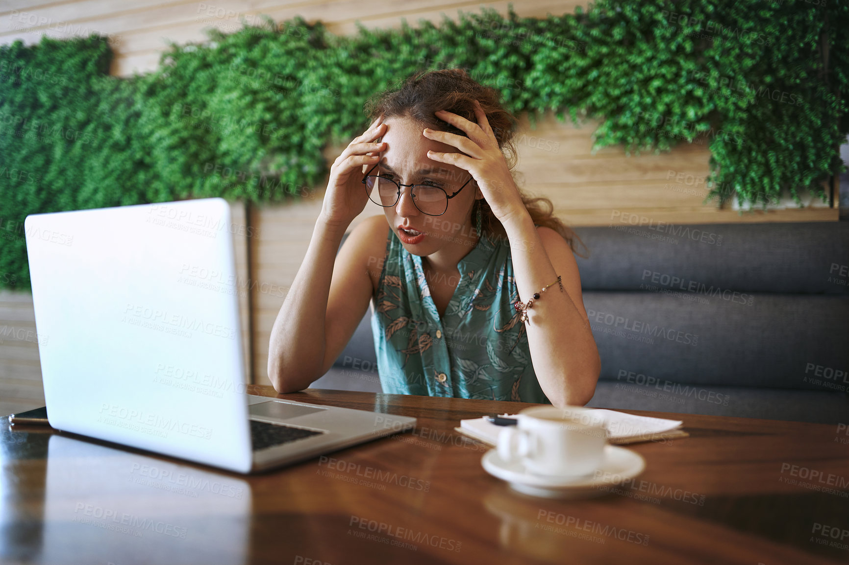 Buy stock photo Shot of a young woman using a laptop and looking stressed while working at a cafe