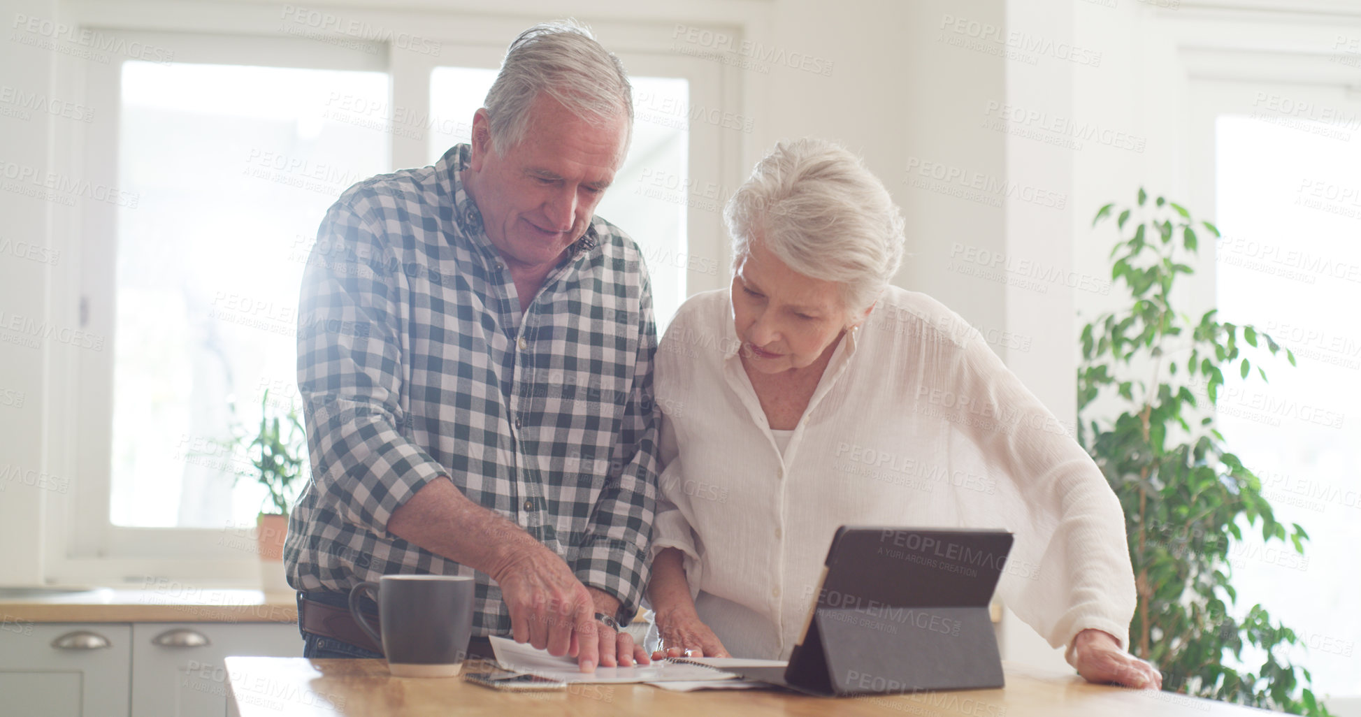 Buy stock photo Cropped shot of a senior couple using a digital tablet while going through paperwork at home