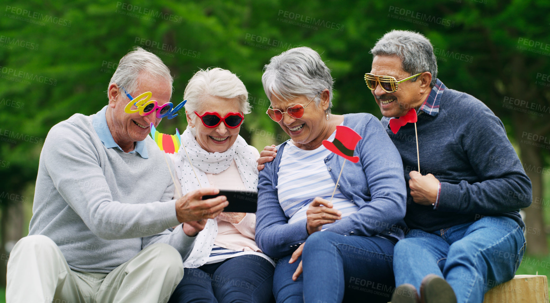 Buy stock photo Shot of a group of happy senior men and women taking selfies while wearing fun glasses at the park