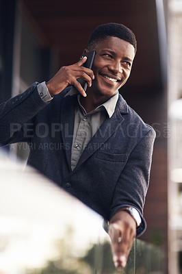 Buy stock photo Shot of a young businessman talking on a cellphone while standing on the balcony of an office