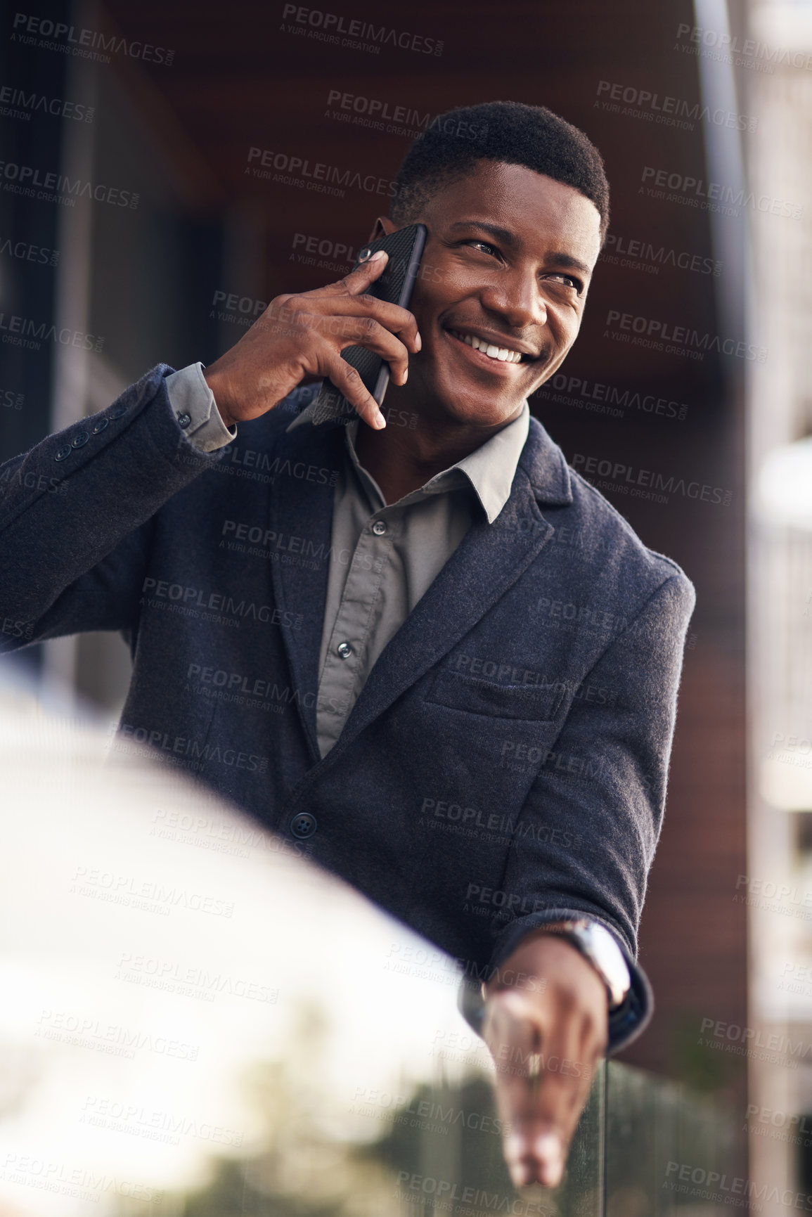 Buy stock photo Shot of a young businessman talking on a cellphone while standing on the balcony of an office