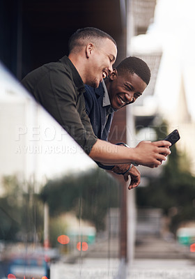 Buy stock photo Shot of two businessman looking at something on a cellphone while standing on the balcony of an office