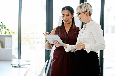 Buy stock photo Shot of two businesswomen using a digital tablet together in an office