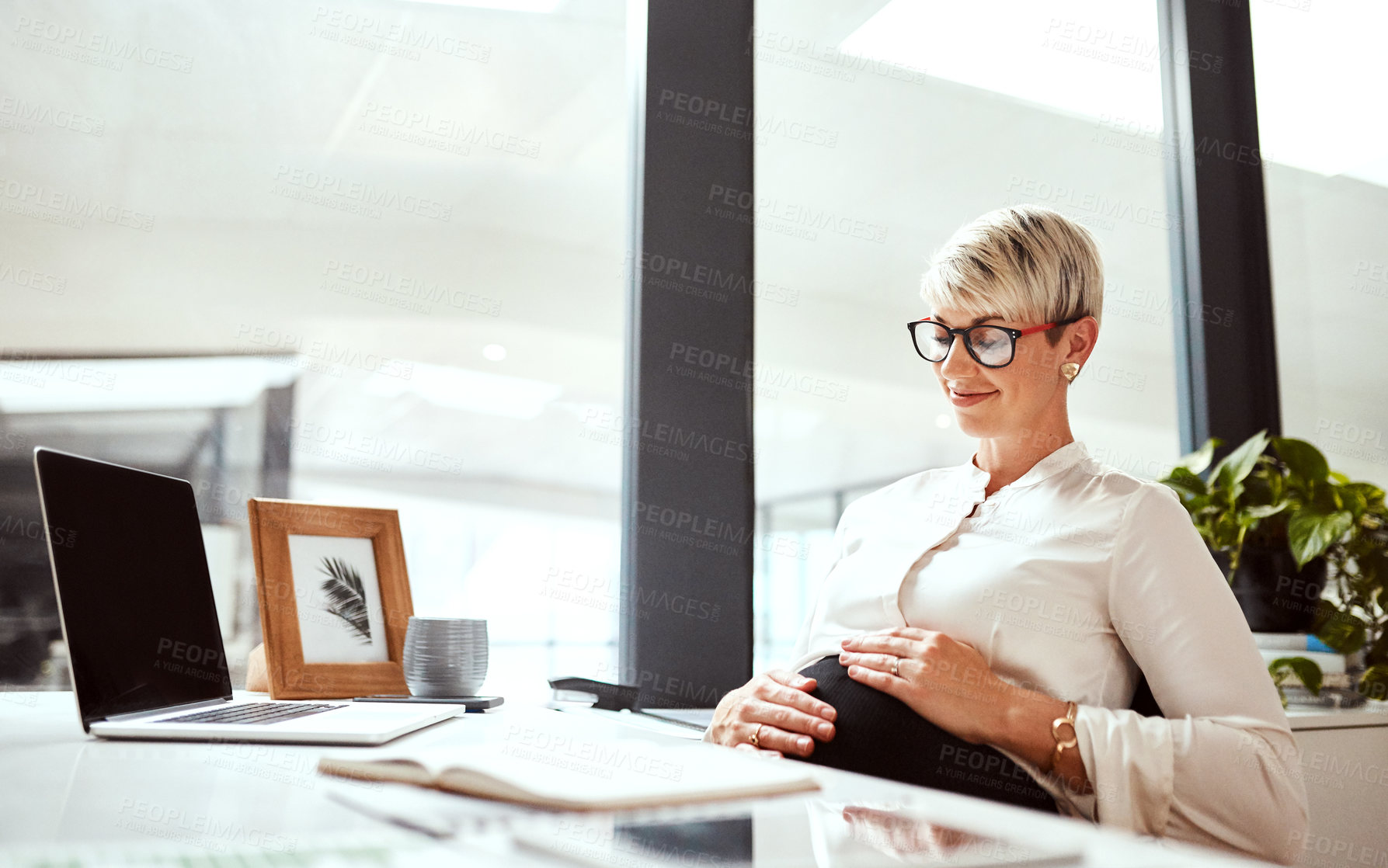 Buy stock photo Shot of a pregnant businesswoman sitting at a desk in an office