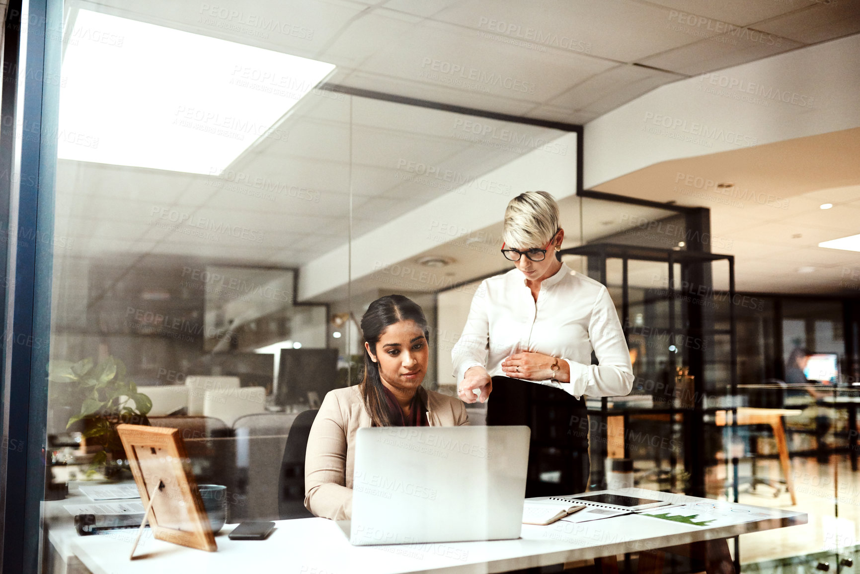 Buy stock photo Shot of two businesswomen working together on a laptop in an office