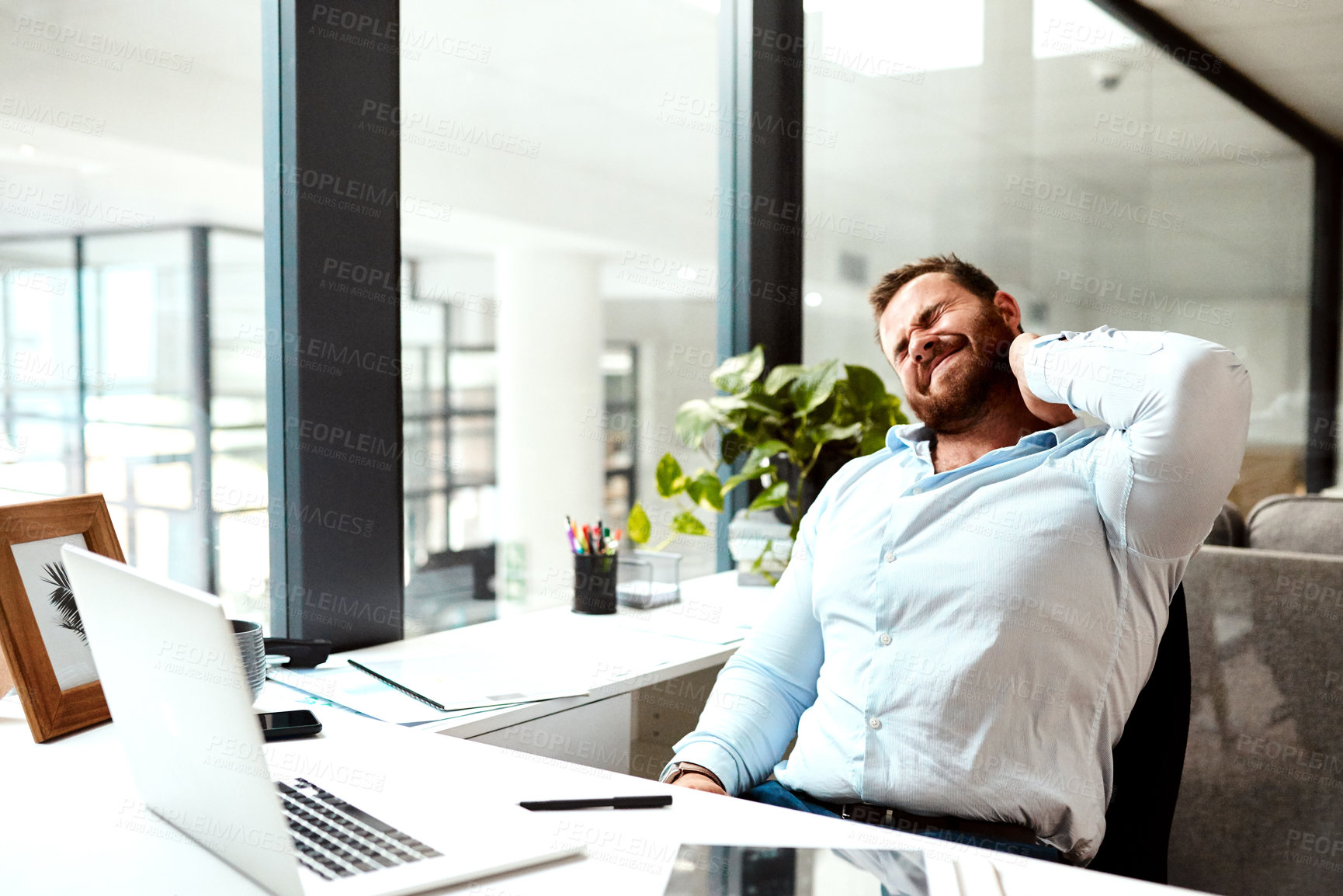 Buy stock photo Shot of a young businessman suffering with neck pain while working in an office