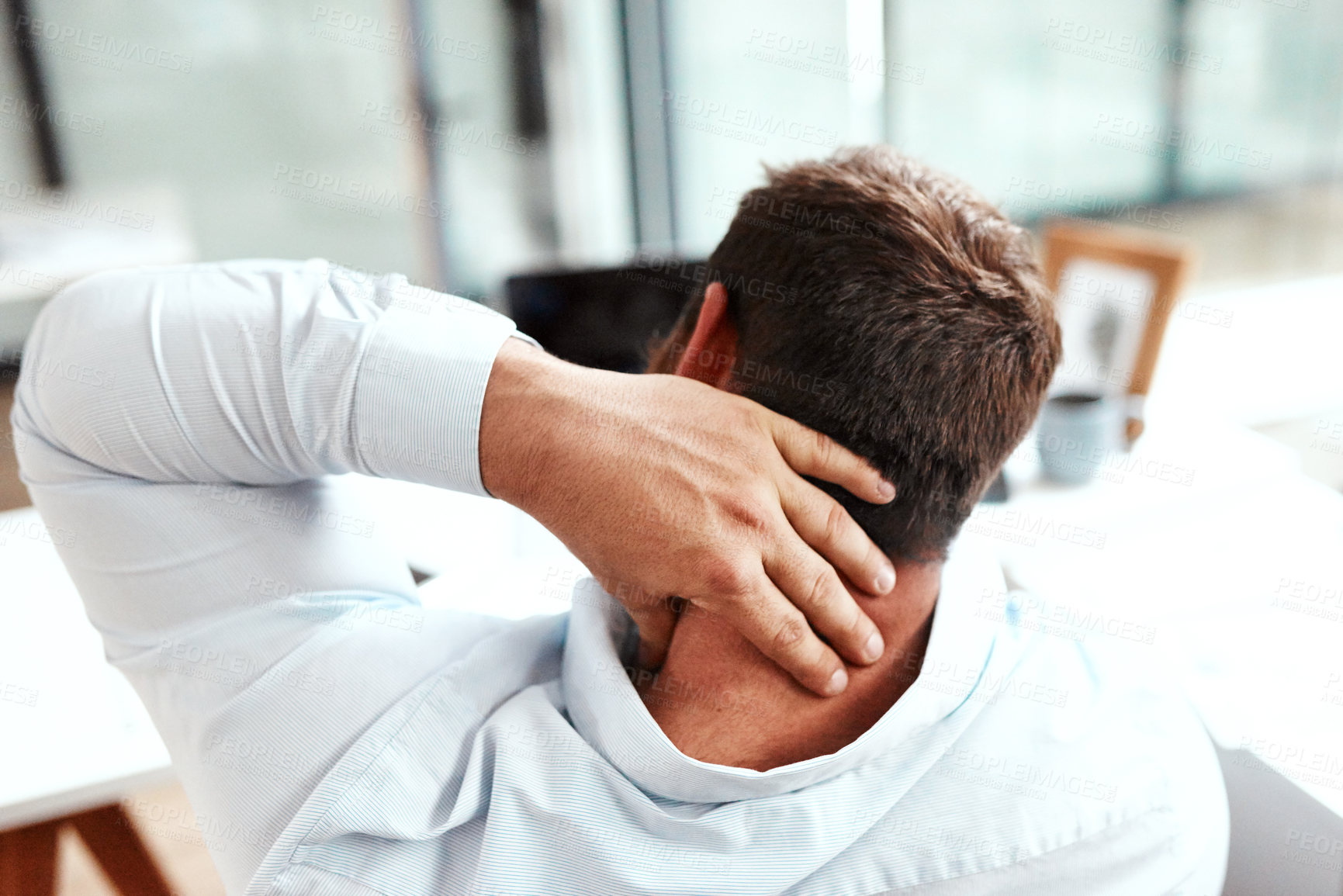 Buy stock photo Rearview shot of a young businessman suffering with neck pain while working in an office