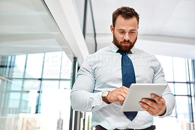 Buy stock photo Shot of a young businessman using a digital tablet in an office