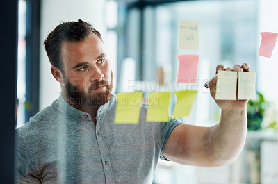 Buy stock photo Shot of a young businessman brainstorming with notes on a glass wall in an office