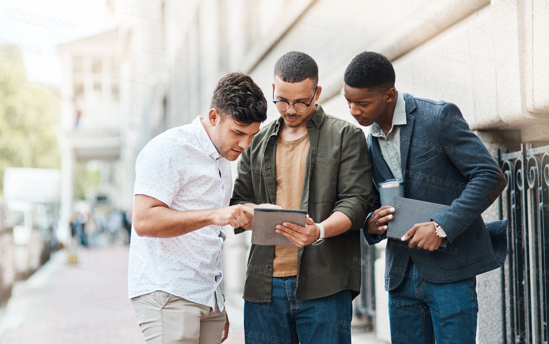 Buy stock photo Shot of a group young businessmen using a digital tablet together against an urban background