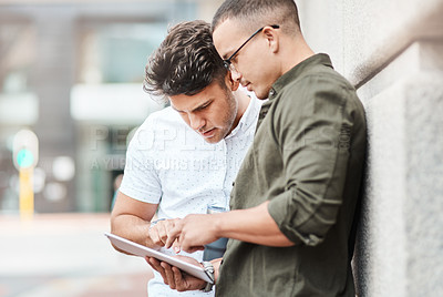 Buy stock photo Shot of two young businessmen using a digital tablet together against an urban background