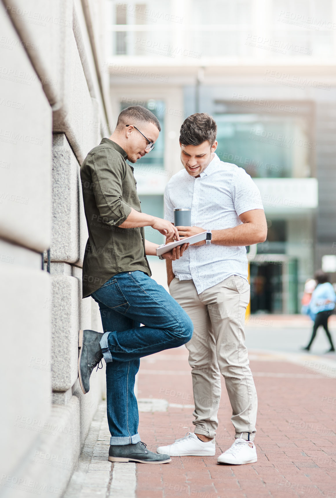 Buy stock photo Shot of two young businessmen using a digital tablet together against an urban background
