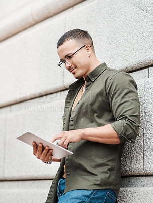 Buy stock photo Shot of a young businessman using a digital tablet against an urban background