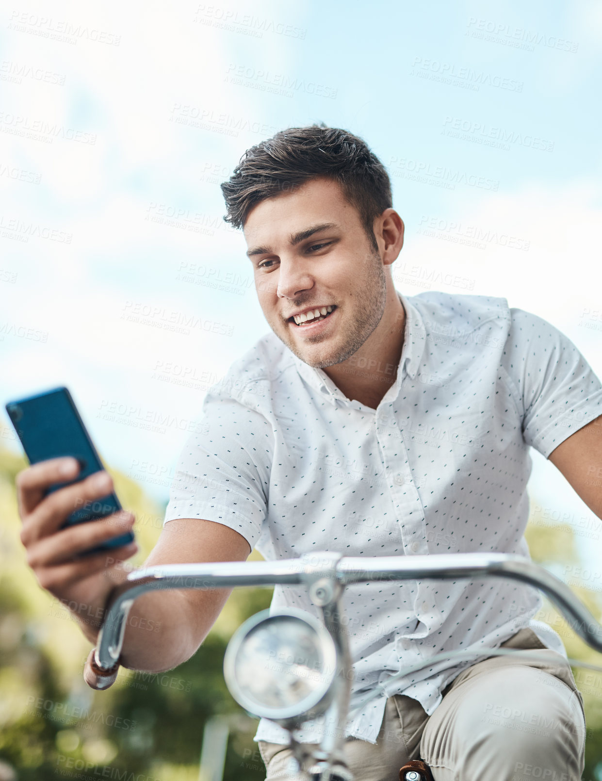 Buy stock photo Shot of a young businessman using a smartphone while riding his bicycle in the city
