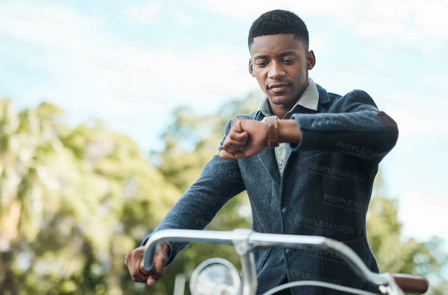 Buy stock photo Shot of a young businessman looking at his watch while riding a bicycle in the city