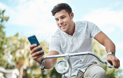 Buy stock photo Shot of a young businessman using a smartphone while riding his bicycle in the city
