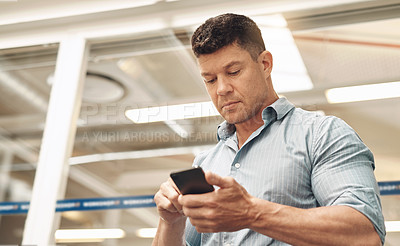 Buy stock photo Cropped shot of a handsome young businessman using his cellphone while standing in the office
