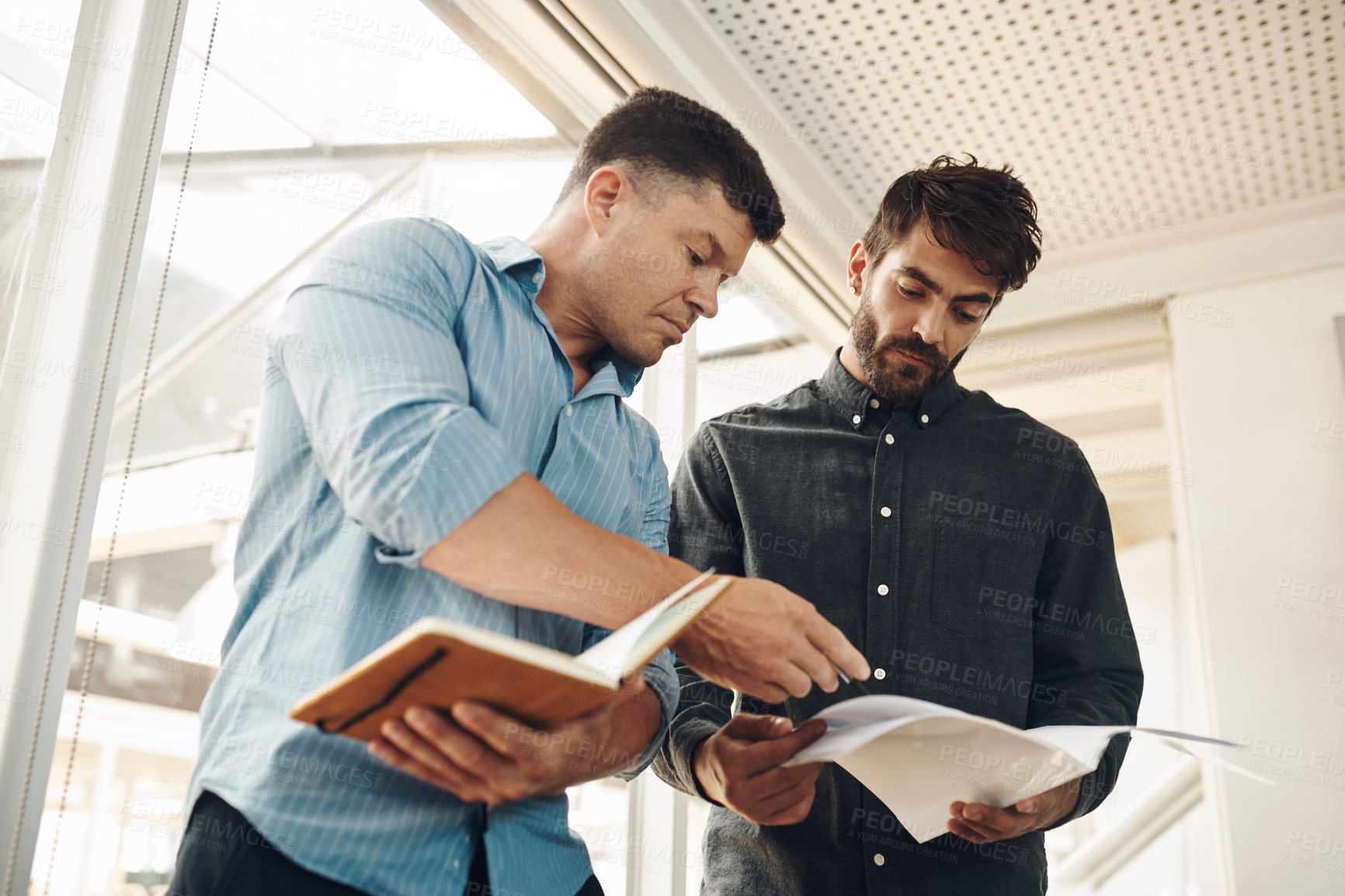 Buy stock photo Cropped shot of two handsome young businessmen looking over their notes after a successful meeting in the boardroom