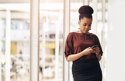 Buy stock photo Cropped shot of an attractive young businesswoman using her cellphone while standing in the office