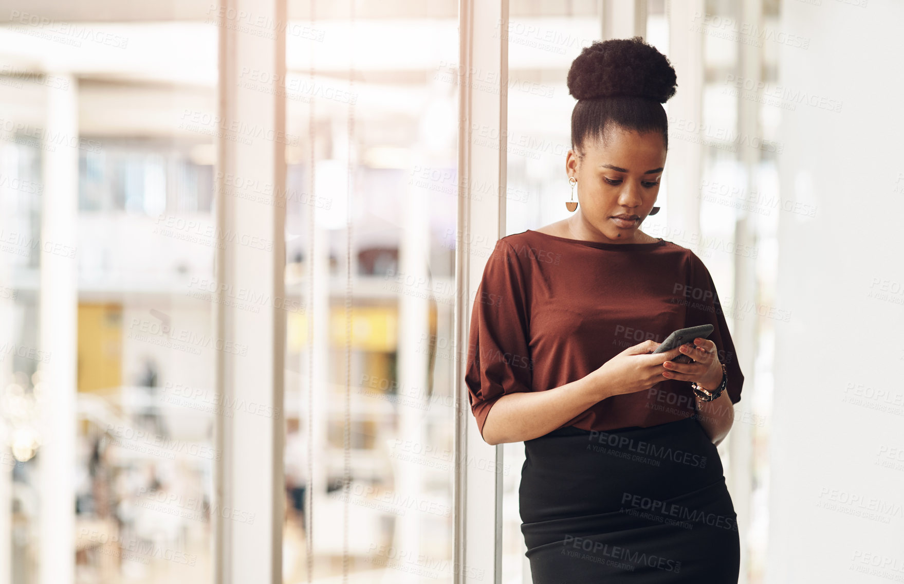 Buy stock photo Cropped shot of an attractive young businesswoman using her cellphone while standing in the office