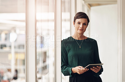 Buy stock photo Cropped portrait of an attractive young businesswoman using her tablet while standing in the office