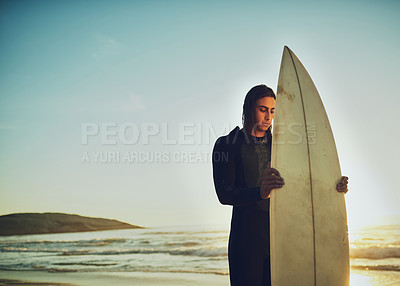 Buy stock photo Shot of a young man standing with a surfboard at the beach