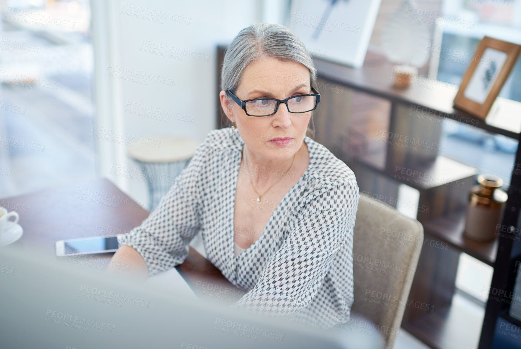Buy stock photo Shot of a mature businesswoman looking thoughtful while working on a computer in an office
