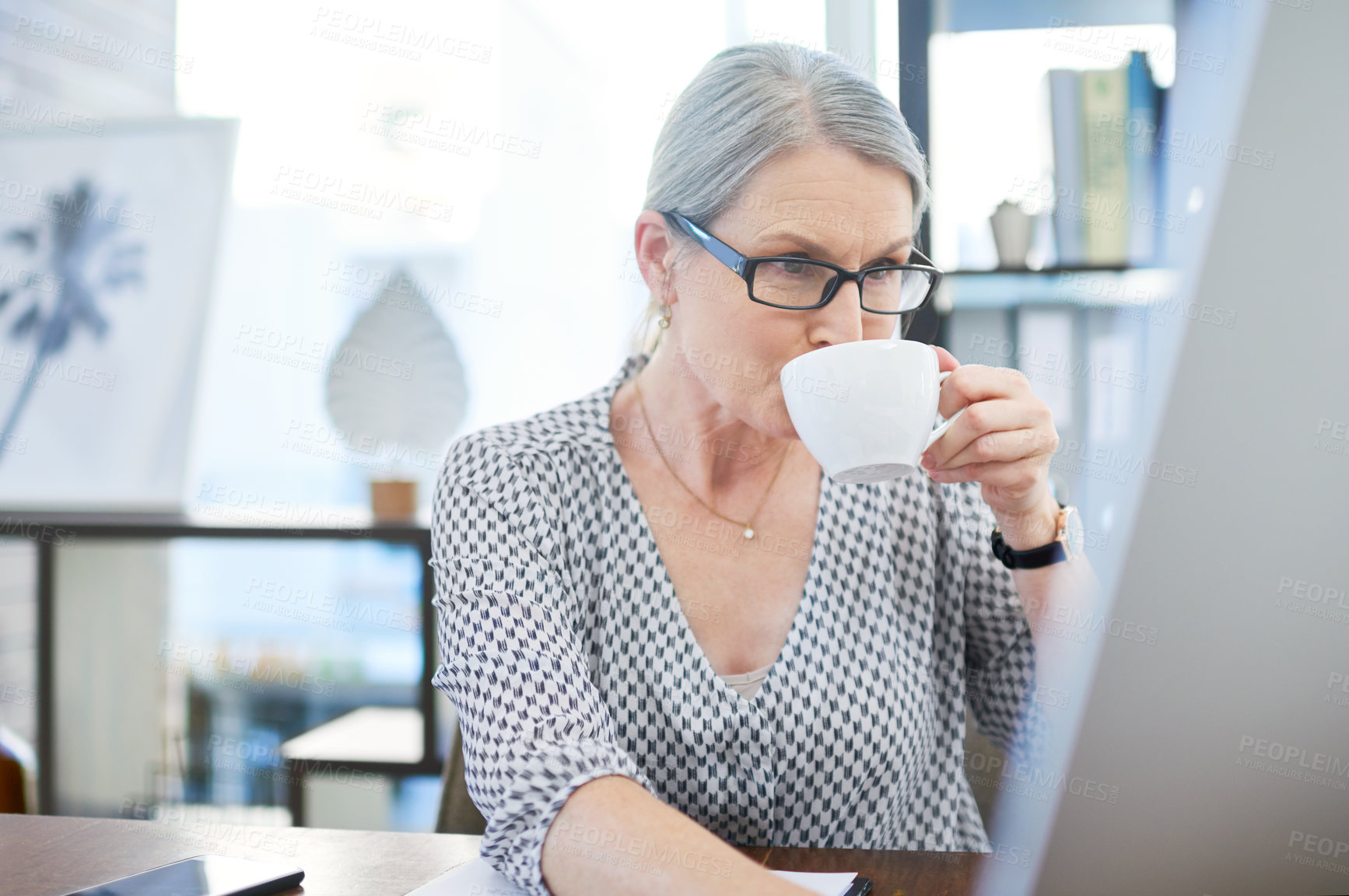 Buy stock photo Shot of a mature businesswoman drinking tea while working on a computer in an office