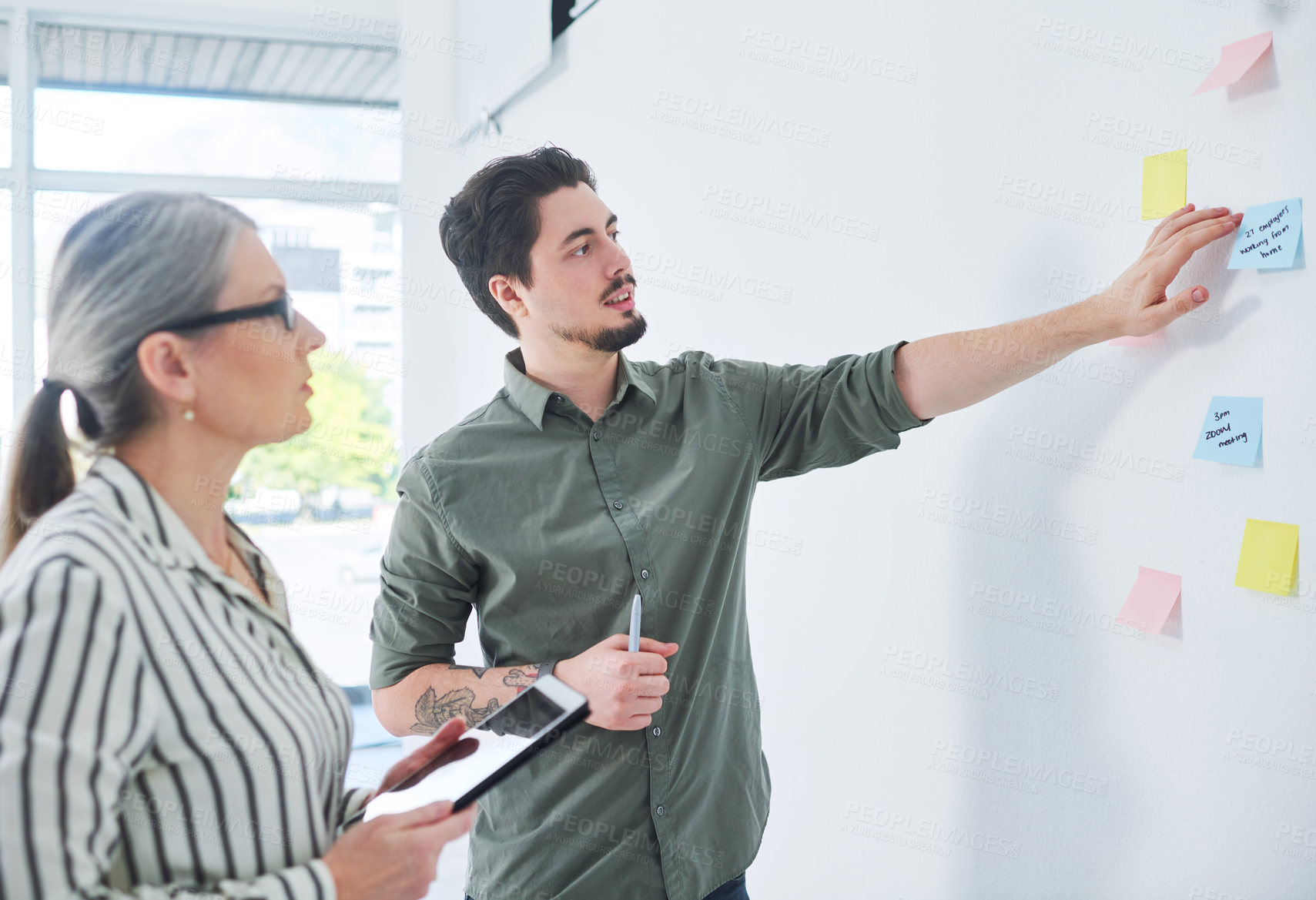 Buy stock photo Shot of two businesspeople brainstorming with notes on a wall in an office