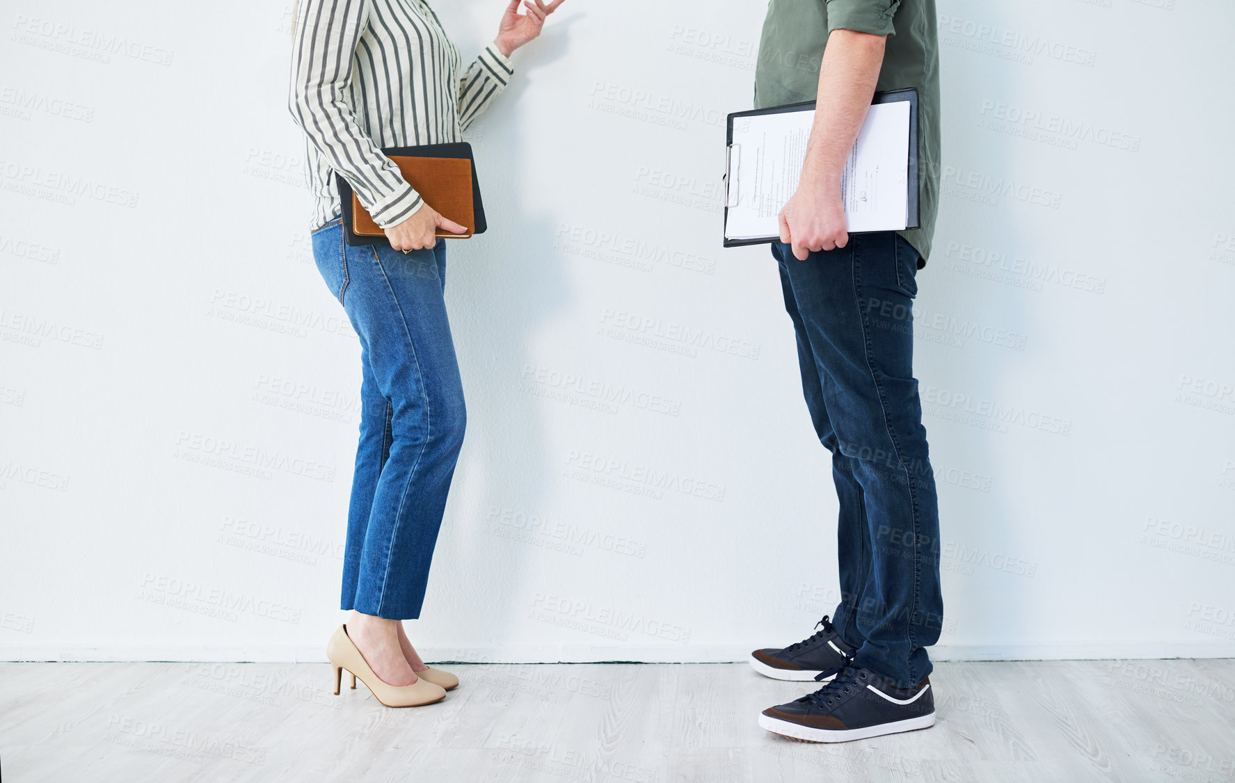 Buy stock photo Closeup shot of two unrecognisable businesspeople having a discussion while standing against a wall in an office