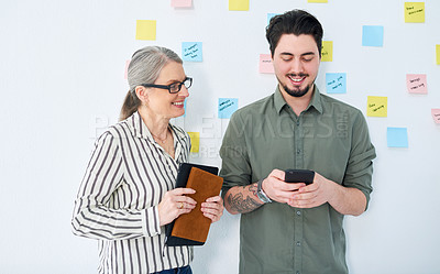 Buy stock photo Shot of two businesspeople using a cellphone together in an office