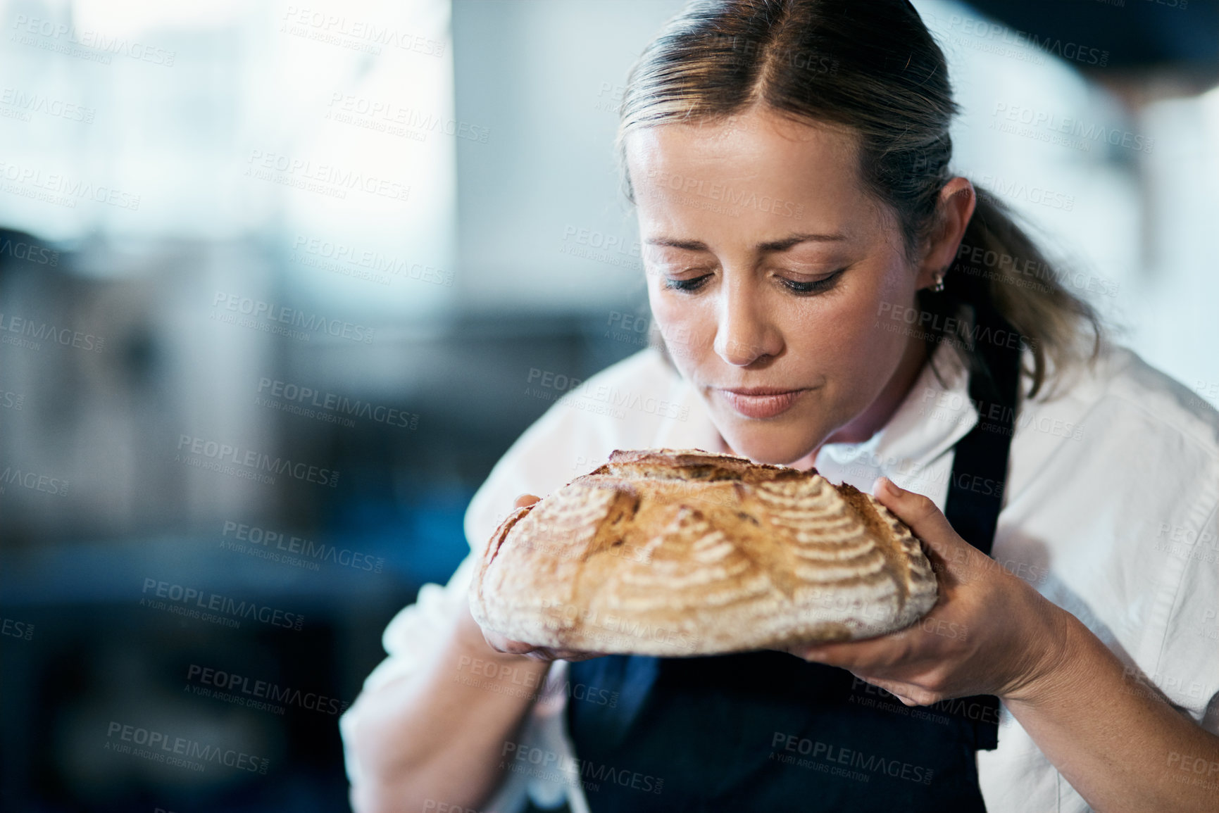 Buy stock photo Baker, pastry chef and cafe owner smelling a loaf of fresh baked bread in the kitchen of her coffee shop. Closeup of a female cook enjoying the aroma of a freshly made dough treat or consumables