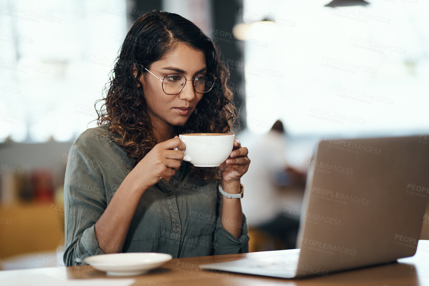 Buy stock photo Shot of a young woman using a laptop and having coffee in a cafe