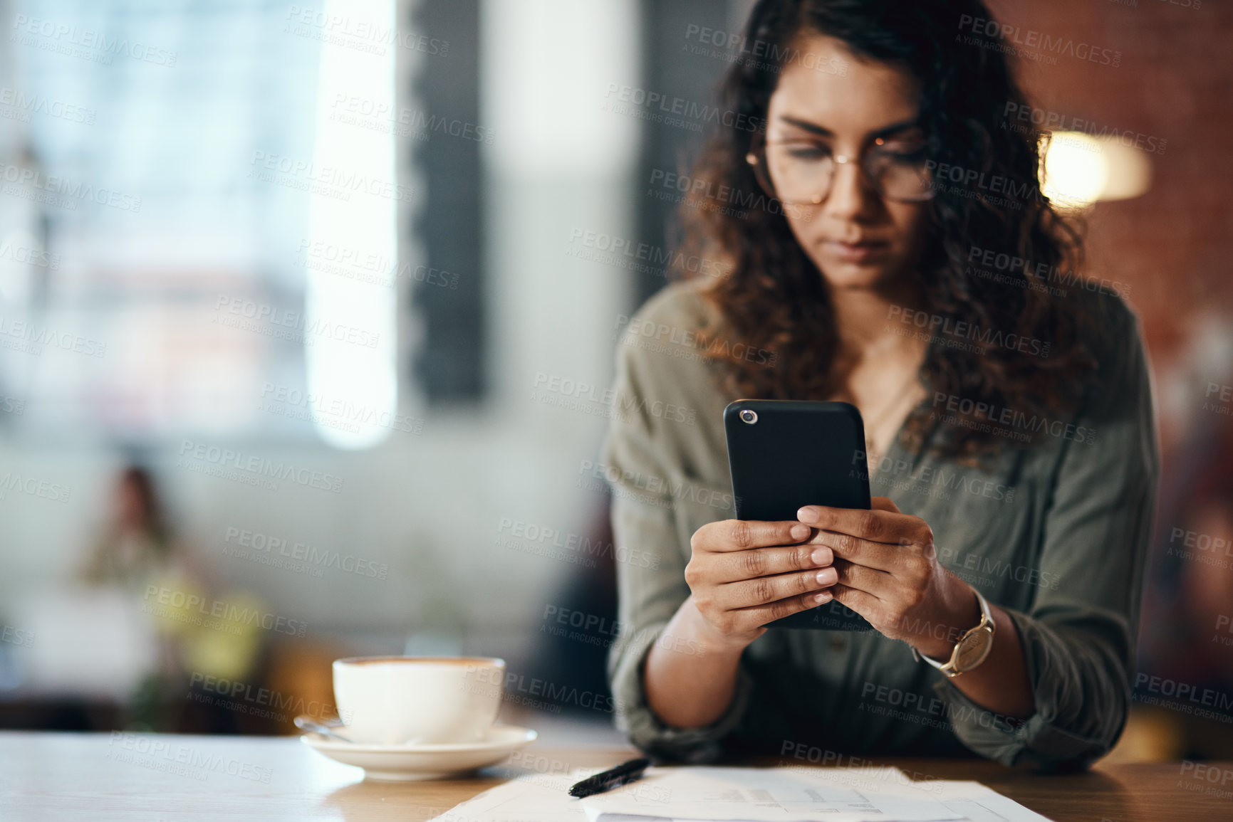 Buy stock photo Shot of a young woman using a smartphone while working in a cafe