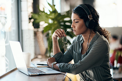 Buy stock photo Shot of a young woman using a laptop and headphones in a cafe