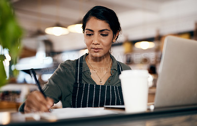 Buy stock photo Small business owner working on a budget in her coffee shop and writing a list of stock to order. Serious female entrepreneur developing a growth strategy for her cafe startup