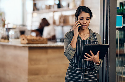Buy stock photo Female cafe business owner using phone talking, ordering and reading on tablet in her store. Serious businesswoman, entrepreneur or employee standing in a coffee shop preparing online grocery order.