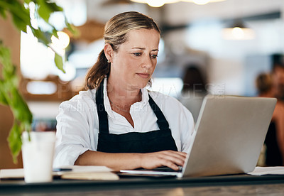 Buy stock photo Shot of a mature woman using a laptop and laptop while working in a cafe