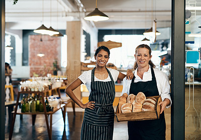 Buy stock photo Shot of two women holding a selection of freshly baked breads in their bakery
