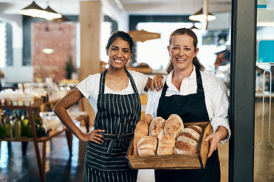 Buy stock photo Shot of two women holding a selection of freshly baked breads in their bakery