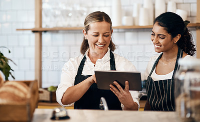 Buy stock photo Shot of two women using a digital tablet together while working in a cafe