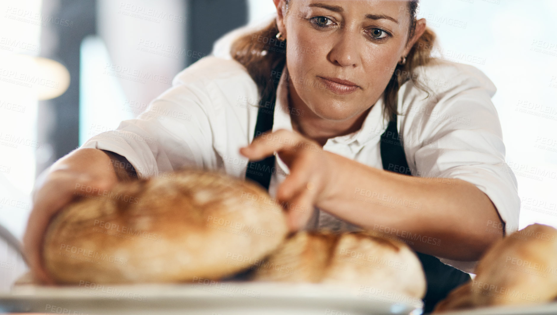 Buy stock photo Shot of a mature woman putting a selection of freshly baked breads on display in her bakery