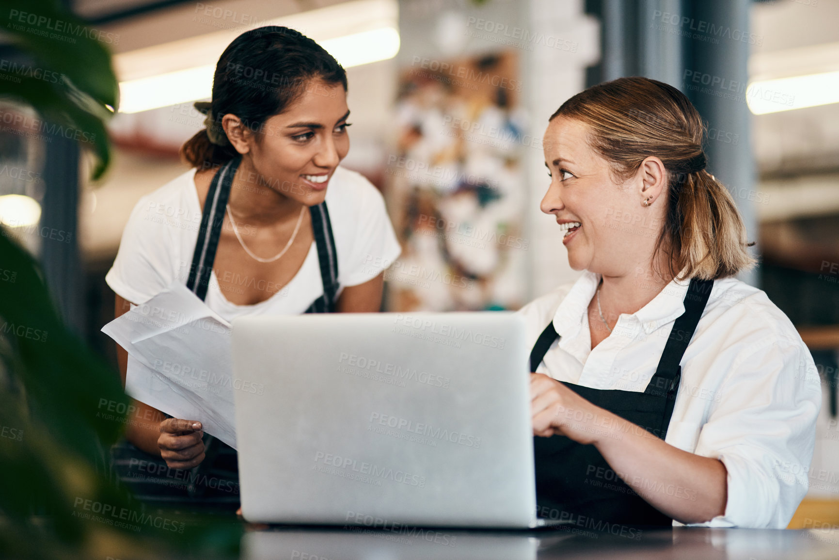 Buy stock photo Small business owner working on a budget strategy or ordering stock online with an employee using a laptop in her store. Female entrepreneur talking to a worker about startup growth and sales