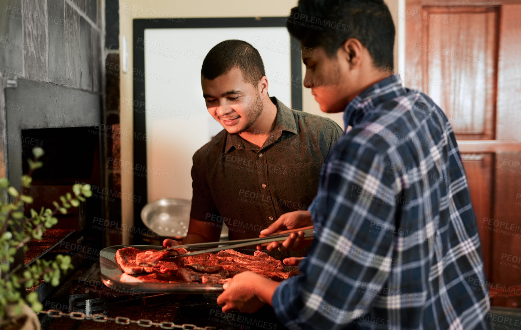 Buy stock photo Shot of two young men grilling meat while having a barbecue