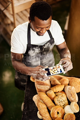 Buy stock photo Cropped shot of a male baker taking a picture on his cellphone of a selection of freshly baked bread