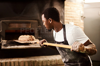 Buy stock photo Cropped shot of a male baker removing freshly baked bread from the oven