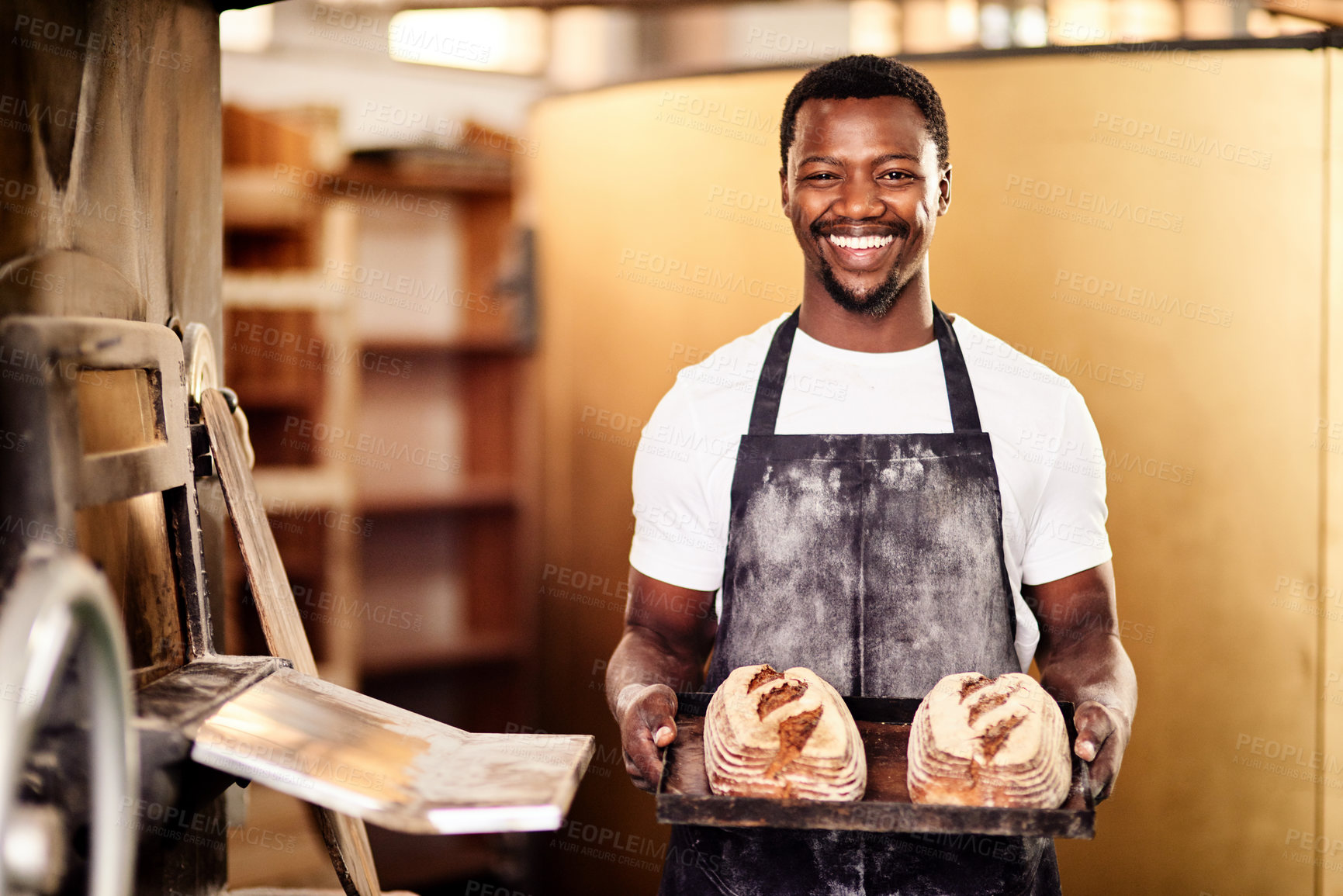 Buy stock photo Cropped shot of a male baker holding up freshly baked bread in his bakery