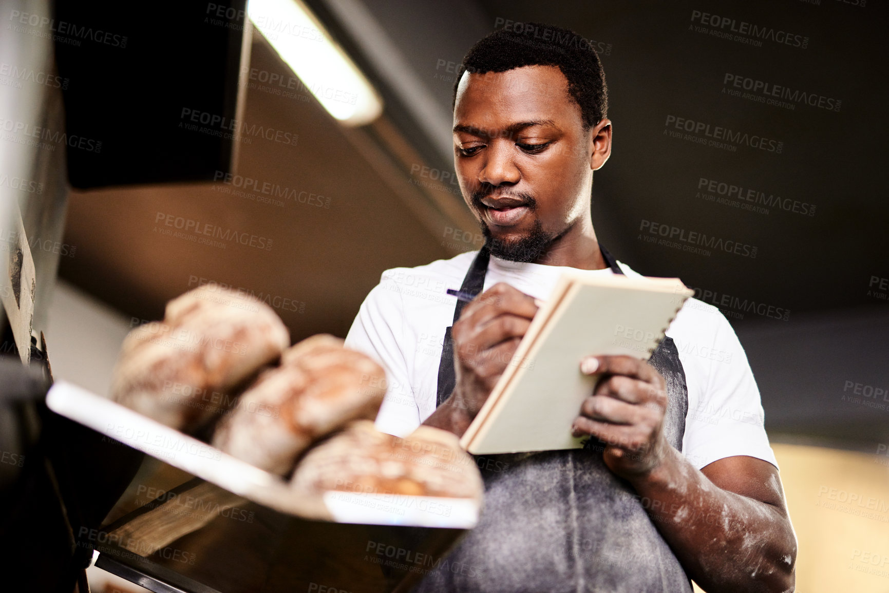 Buy stock photo Cropped shot of a male baker making notes while working in his bakery